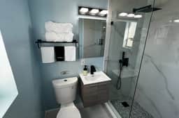 Modern spacious shower with rain shower overhead and Handheld Sprayer. We provide toiletries such as shampoo, conditioner, shower gel and hand soap. Fluffy large bath towels are on the rack.
