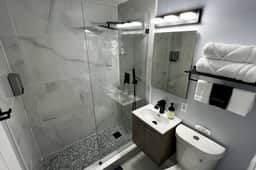 Modern spacious shower with rain shower overhead and Handheld Sprayer. We provide toiletries such as shampoo, conditioner, shower gel and hand soap. Fluffy large bath towels are on the rack.